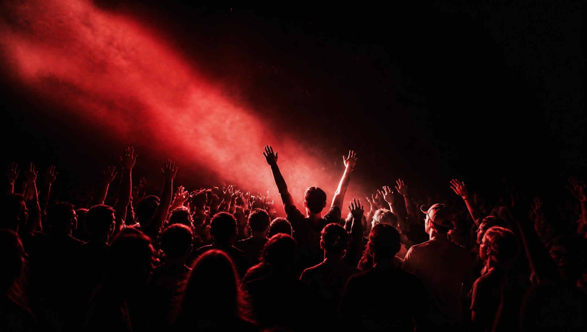 A crowd with arms raised under a beam of red light